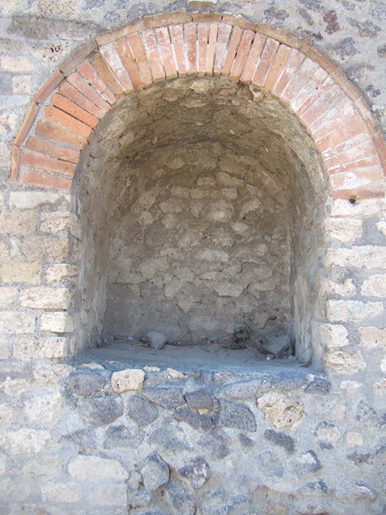 Pompeii II.4.7a. September 2005. Street shrine at east end of II.4 on Via dell’Abbondanza.
Compital aedicula shrine.
When excavated in 1912, the following description was given in the Notizie degli Scavi:
Opening on to the public street pavement was an important sacellum with an arched niche 1.22m tall, 1.06m wide and 1.08m deep.
It was ornamented above with a beautiful cornice in stucco plaster.
The niche was a small temple in which were venerated the Penates or the protecting divinities in Pompeii.
Two large holes with splinters of wood still attached were found in the floor of the shrine.
It was thought these were to anchor the figures of the Lares Compitales or were bases for them to stand on.
The statues had vanished, perhaps taken by ancient robbers who had cut a hole through the upper left corner of the shrine.
This damaged the decorative cornice and stucco relief on the façade.