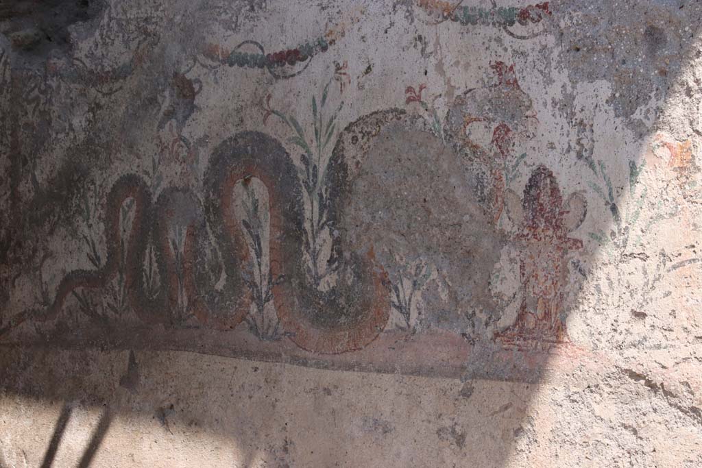 V.8, Pompeii. September 2021.
Looking east towards painted street shrine at the rear of the Well, on north side of Vicolo delle Nozze d’Argento. Photo courtesy of Klaus Heese.
A serpent approaches a marble painted altar from the left. On the altar there appears to be a pinecone and two eggs.
In the background are flowering plants while above and on the left side are garlands.