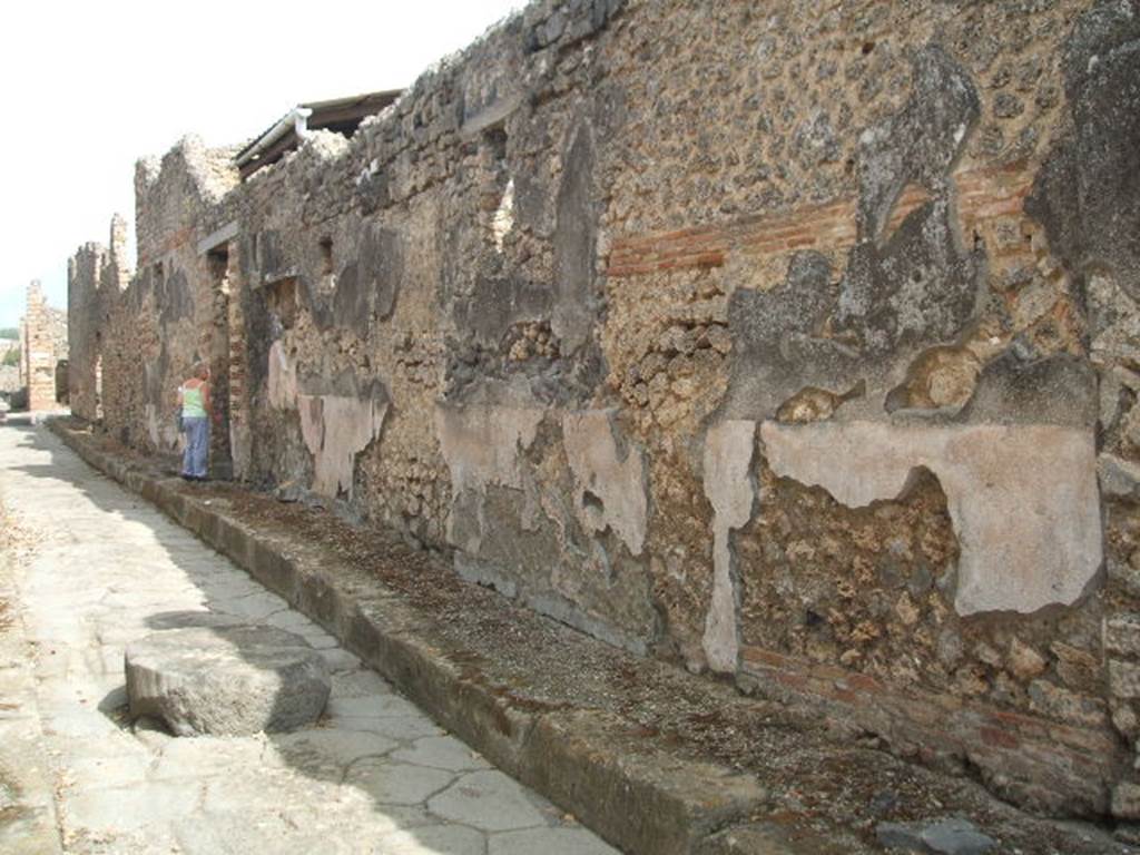 Vicolo di Tesmo looking north past remaining painted plaster on walls outside IX.7.20.
On the exterior wall of IX.7.20, opposite the doorways of IX.2.17/18, a large painted lararium was found.
According to Trendelenburg, this stood out because of the freshness and strength of the colours.
It was divided into two parts, of differing sizes. The upper part was 1.47m wide and the lower part was 4.12m wide.
The upper part showed the two Lares.
In the middle between them was the Genius with cornucopia, dressed in a white tunic holding a patera above a flaming altar.
Behind the altar was the figure of small tibicen who played the double pipes.
Suspended above were two garlands and above the garlands appeared the bust of Luna on the left and a bust of Sole on the right.
The lower part showed a tall altar in the centre and three heads of Medusa.
Two serpents approached the altar, one from each side.
See Trendelenburg in BdI 1871, pp. 199-200.
See Sogliano, A., 1879. Le pitture murali campane scoverte negli anni 1867-79. Napoli: Giannini. (p.14, No. 33).
See Fröhlich, T., 1991. Lararien und Fassadenbilder in den Vesuvstädten. Mainz: von Zabern. (F65, p. 335)