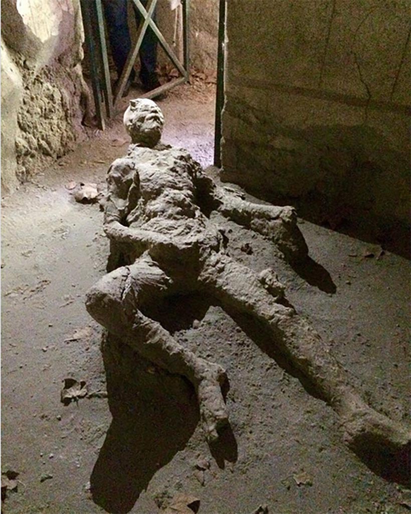 Victim 67. Male victim aged over 20 years.
Photograph © Parco Archeologico di Pompei.
Found in room 28 of VII.16.17 Casa di Maius Castricius between 1958 and 1980.
Traces of fabric are recognizable especially on the right shoulder and legs.
He was probably wearing a short tunic with three-quarter sleeves.
On the right tibia there are traces of fabric perhaps belonging to a bandage to plug a wound.
The position has always remained the same, that is, room 28 of VII.16.17 Casa di Maius Castricius.
See Osanna, N., Capurso, A., e Masseroli, S. M., 2021. I Calchi di Pompei da Giuseppe Fiorelli ad oggi: Studi e Ricerche del PAP 46, p. 476-7, Calco n. 67.
The victim was found in the southwest corner of room 28.
See Varriale I., 2006. in Aoyagi M. and Pappalardo U., 2006. Pompei (Regiones VI-VII) Insula Occidentalis. Napoli: Valtrend, p. 476.
