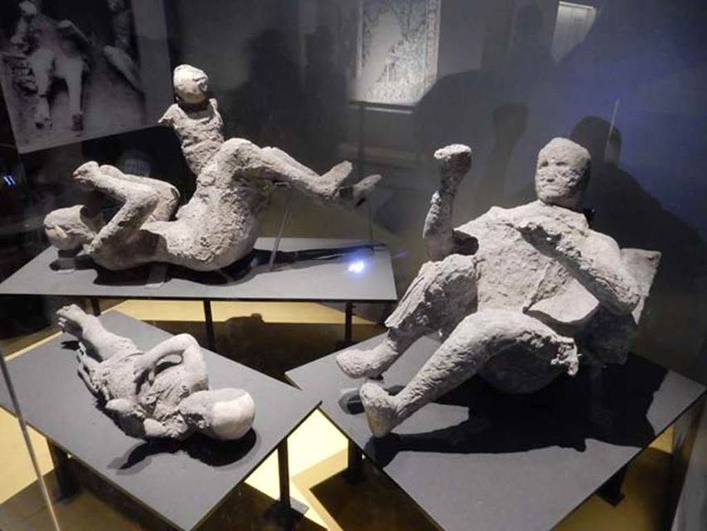 VI.17.42 Pompeii. Victims 50 to 53, May 2018. 
Plaster casts of fugitives found in the lower corridor, see VI.17.42, Lower and Garden, for area. Photo courtesy of Buzz Ferebee.
Experts had previously made assumptions about the victims' identities and relationships, but new DNA evidence counteracts their long-held theories.
Inside the House of the Golden Bracelet, three people were discovered at the foot of the staircase - the location gets its name from the jewellery one of the two adults was wearing. This, in addition to the adult being found with a child on their hip, caused experts to believe this victim was a mother of two and the father was the second adult.
But this isn't the case, according to scientists in Italy, Germany and the US as written in the Current Biology journal 2024, as the victim sporting the bracelet was actually found to be a dark-haired, dark-skinned male and he has no relation to the two infant boys found with him, while genetic evidence also appears to point to the second adult also being a male too.
Meanwhile, all three had various eastern Mediterranean or North African origins.
Andrew Wallace-Hadrill, a professor at the University of Cambridge who wasn't involved in study noted how this new DNA evidence "turns some older interpretations, especially those based on rather romantic assumptions, on their head".
He also commented on how this evidence reflects the society at the time.
"One would predict, in a society heavily based on slavery, a significant diversity." 
“It is very interesting for instance they have identified an individual with dark skin and black hair, which strongly points to an enslaved person from Africa.”

