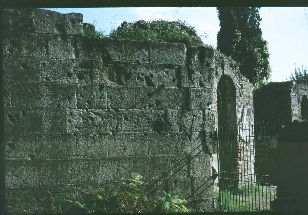 Pompeii Porta Ercolano or Herculaneum Gate east side. Looking south towards city walls.
Photographed 1970-79 by Günther Einhorn, picture courtesy of his son Ralf Einhorn.
See Notizie degli Scavi, 1943, (p.275-294),
for article entitled “Isolation of the wall between the Vesuvian Gate and Herculaneum Gate.”
(Isolamento della cinta murale fra Porta Vesuvio e Porta Ercolano).
According to Van der Graaff –
“Littered with scars from the Sullan siege, the fourteen-course section still displays some of the highest-quality finished masonry of the entire circuit (Note 75). It is also unique as the only stretch of fortifications composed entirely of tuff – a circumstance reflecting its prominent position next to the gate……….
The resulting effect set the stage for approaching viewers of the architectural character of the city behind the gate.”
See Van der Graaff, I. (2018). The Fortifications of Pompeii and Ancient Italy. Routledge, (p.65 and Note 75).