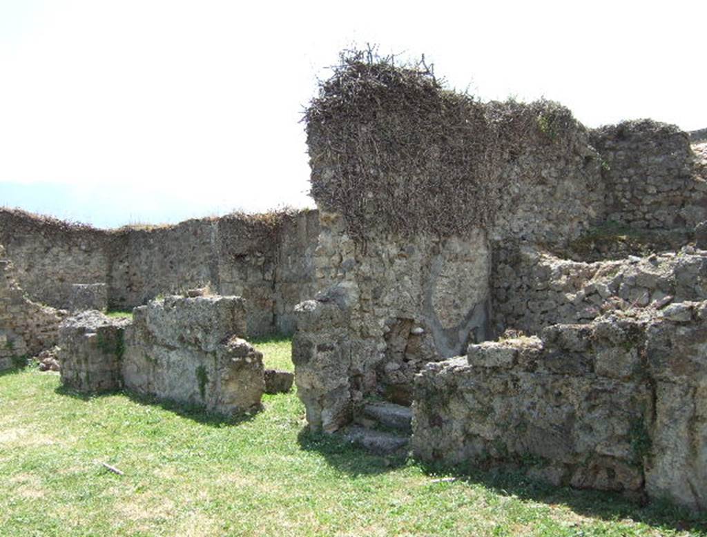 VII.12.3 Pompeii. May 2006. Rooms on west side of atrium.
According to Eschebach, on the right side of the atrium were steps to the upper floor, these are on the right of the photo above.
On the left of the photo, there was a windowed triclinium with a wide opening onto the north portico of the garden.
Also, on the right of the atrium was a lararium.
See Eschebach, L., 1993. Gebäudeverzeichnis und Stadtplan der antiken Stadt Pompeji. Köln: Böhlau. (p.326)
According to Boyce, on the west side of the atrium Fiorelli reported a larario; but now there only remains a ruined brick base.
This may have supported an aedicula.
See Boyce G. K., 1937. Corpus of the Lararia of Pompeii. Rome: MAAR 14. (p.70, no.312).