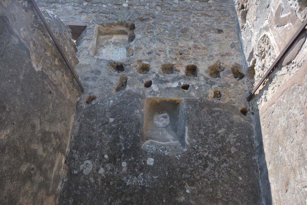 IX.5.2 Pompeii. May 2017. Room ‘q’, looking towards upper west wall and upper floor, with rectangular niche.
Foto Christian Beck, ERC Grant 681269 DÉCOR.
According to Boyce –
in the west wall of a room on the upper floor, above the first room on the west side of the peristyle, was a rectangular niche (h.0.60, w.0.50, d.0.28).
On its back wall was painted the figure of Vesta (or Epona?), seated upon an ass (or with an ass nearby).
The account in the Not. Scavi describes the two serpents at an altar painted below the niche, though they are not mentioned by either Sogliano or Mau.
The layer of stucco upon which the figure of Vesta was painted has fallen away, partially revealing beneath it an earlier layer, upon which can still be seen two standing figures, each wearing a green garment and having a large yellow bulla suspended from his neck; they are both alike and their posture suggest that of the Lares.
See Boyce G. K., 1937. Corpus of the Lararia of Pompeii. Rome: MAAR 14. (p. 85, no. 420).
See Giacobello, F., 2008. Larari Pompeiani: Iconografia e culto dei Lari in ambito domestico. Milano: LED Edizioni, (p.206, no.100).