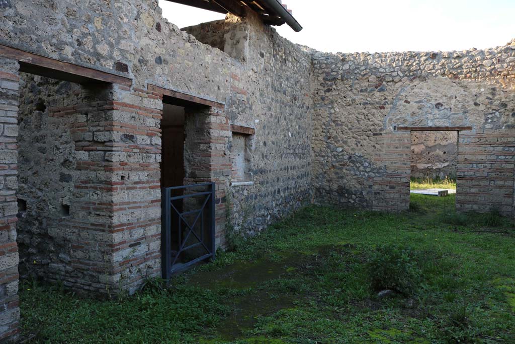 IX.5.16 Pompeii. December 2018.
Looking north across atrium a’ from entrance doorway, on right is the doorway into the atrium “b” of IX.5.14.
On the left (west) side of atrium a’, on the left, is the doorway to kitchen and latrine e’.
Centre left, is the doorway to cubiculum f’. Photo courtesy of Aude Durand.
According to Boyce, on the south wall of the kitchen was a large rectangular panel (h.1.0 w.2.0) of white stucco.
On it were painted two yellow serpents with red crest and beards.
These were on either side of a tile embedded and projecting from the wall.
A fire was painted on the wall above the tile.
The background was painted with plants, and across the top were two painted garlands.
On each of the garlands was a painted bird.
See Boyce, G. K., 1937. Corpus of the Lararia of Pompeii. Rome: MAAR 14. (p. 86, no. 425)
See Giacobello, F., 2008. Larari Pompeiani: Iconografia e culto dei Lari in ambito domestico. Milano: LED Edizioni, (p.208, no.102)