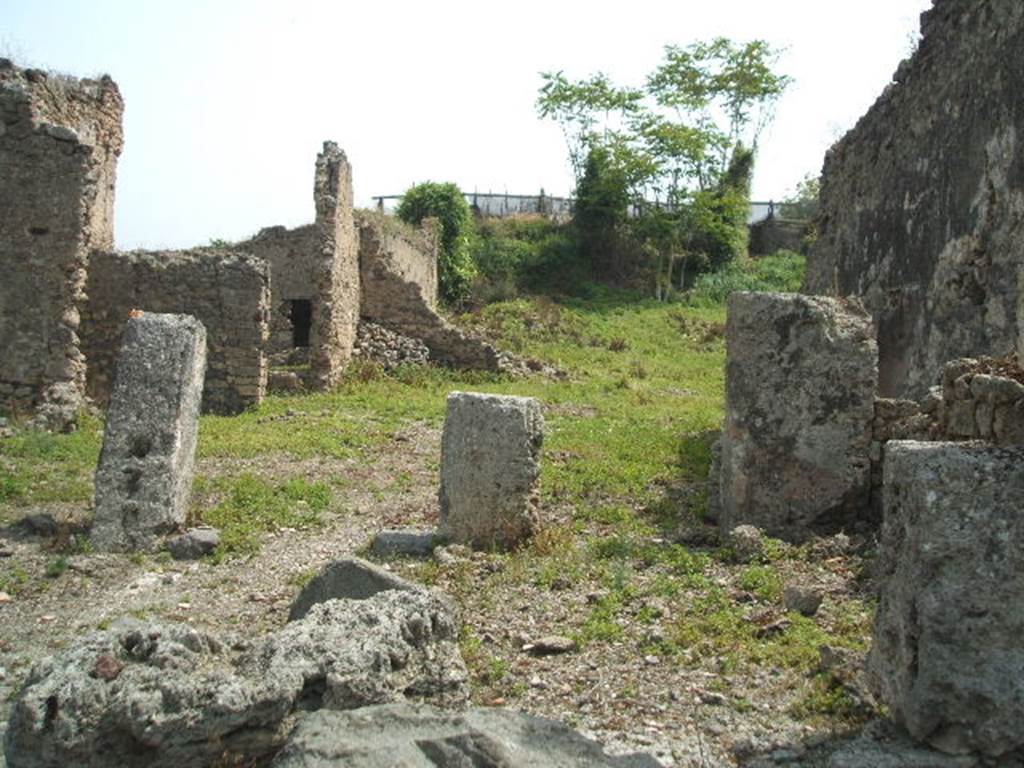 IX.6.4 Pompeii. May 2005. Looking east across site.
The eastern extent of the house can be seen across the centre of the photo, in the middle left.
The pile of stones in the middle centre of the picture, against the north-east wall of the kitchen, would be the site of the hearth, with site of lararium painting above it.
The wall with a doorway in room “z”, leading to the peristyle of IX.6.5, can be seen in the wall on the left.
According to Boyce –
In the small open courtyard behind the tablinum in the south wall is an arched niche (h.0.32, w.0.27, d.0.25, h. above floor 2.10).
In its floor was a depression and in the vault of the ceiling a hole; it is called by the Not. Scavi – la piccola nicchia dei Penati.
In the kitchen behind this court, in the north-east corner stands the hearth and on both walls above it is the lararium painting (h.055).
On the north wall is the Genius with cornucopia and patera, pouring a libation upon an altar furnished with offerings, around which serpent is coiled. On the east wall is a burning altar and on each side of it stands a Lar with rhyton and patera.
See Boyce G. K., 1937. Corpus of the Lararia of Pompeii. Rome: MAAR 14. (p.86, no.429 & 430).
According to Garcia y Garcia, during the night bombing of 16th September 1943, the prothyron, the atrium and four nearby rooms adjoining the south and south-west of this house were hit by a bomb. The pavement and street outside were also damaged.
Another bomb destroyed a good part of the large room on the east of the house and the perimeter eastern wall of the room on the north-east.
See Garcia y Garcia, L., 2006. Danni di guerra a Pompei. Rome: L’Erma di Bretschneider. (p.153).