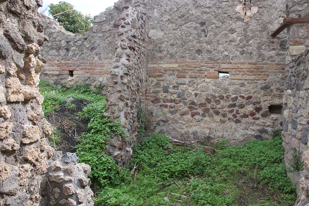 IX.7.16 Pompeii. October 2024.
Room “d”, on south side of room 3, on right, looking south through site of wall and doorway into kitchen, no longer in situ.
On the left would be a doorway into room 6. Photo courtesy of Klaus Heese.
According to Boyce –
“In the kitchen, which is entered through the first room on the right of the atrium, on the north wall to the right of the entrance and on the west wall, is the lararium painting (h.1.50, w. on north wall 0.60, on the west wall 1.94): on the right of an altar stands the Genius in the usual attire, pouring a libation from a patera; on the left is the lower part of the figure of the tibicen and behind him stands a camillus wearing white tunic and carrying in his left hand, a shallow dish, taeniae in the right hand. Behind the Genius the popa, wearing a crown of leaves, holds a knife to the throat of a hog adorned with a red band around its belly. On each side of this group of four is a Lar in the usual attire. In the lower zone two yellow serpents, each with red crest, are confronted at an altar. The painting thus described is all on the west wall of the room. On the north wall are painted the following kitchen objects (from top to bottom): a hearth, an uncertain object – perhaps the fire-wood for the hearth – a hog’s head, a pot on a fire.
Traces of the older lararium painting, not entirely covered over by the later, are to be seen on the west wall, where the figure of a Lar can be made out on the left side.”
See Boyce G. K., 1937. Corpus of the Lararia of Pompeii. Rome: MAAR 14. (p. 87, no. 436)
and Boyce gives the reference Bullettino dell’Instituto di Corrispondenza Archeologica (DAIR), 1883, 145.