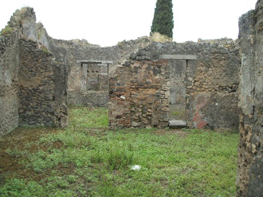 IX.9.12 Pompeii. May 2005. Looking west across room 11, the central courtyard room.
According to Boyce – on the left in the south-west corner a sacrarium was built by running a wall parallel to the south wall, and extending 1.14 from the west wall, and covering the enclosure with a sloping roof (height varies from 1.60 to 2.0).
At the east end of this sanctuary stood a small altar of tufa (0.50 by 0.40, h.0.60) originally coated in stucco.
The inside surface of the north wall is decorated upon a white ground with a line-drawing: an aedicula and within it a male figure, standing clad in a yellow, tunic-like garment, the front of which is white between two red stripes running vertically from shoulder to hem; his flesh is reddish; in his left hand he holds a palm (?) branch at the level of his waist, in his right hand three taeniae; around his head is a fillet. The opposite south wall is also covered with white stucco, the west wall with a coarser variety.
Near the sacellum was found a female head of terracotta (h.0.17) with idealized features,
apparently part of a statue.
He quotes reference Not. Scavi, 1889, 136, 1891, 255.
See Boyce G. K., 1937. Corpus of the Lararia of Pompeii. Rome: MAAR 14. (p. 92-3, no.464).