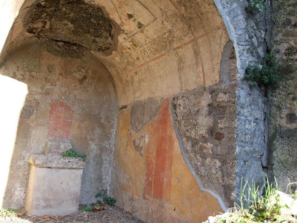 HGE12 Pompeii. December 2006. Lararium with altar, south and east wall. According to Boyce, in an open court was a sacrarium, apparently dedicated to Hercules and Bacchus. Upon the yellow background of the rear wall of a deep niche were painted the attributes of Hercules – a large skyphos and a club. In the pediment on the wall above the niche was painted the figure of Bacchus, accompanied by two flying cupids holding a wreath, one on each side of him. See Boyce G. K., 1937. Corpus of the Lararia of Pompeii. Rome: MAAR 14. (p.97, no.479)