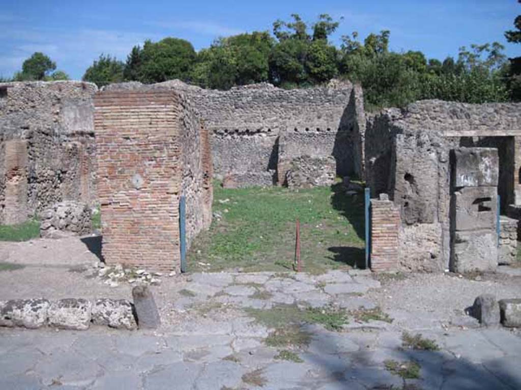 I.1.3 Pompeii. September 2010. Entrance, looking east across Via Stabiana.
Photo courtesy of Drew Baker.
According to Warscher, quoting Mau in Bull. Inst 1875, p.27, “Per lasciar entrare i carri il marciapiede è interrotto avanti alla porta, e il selciato della strada continuato fino all’ingresso che è largo come quelli delle botteghe ed era chiuso mediante una porta a due partiti. La porta però non si fermava come al solito: nel bel mezzo della soglia di lava vi sono gli avanzi d’un uncino di ferro, e più a sinistra la buca per un chiavistello solo, mentre l’altro partito ne stava senza. Invece al di fuori della porta si trovano nella soglia quattro buche quadrangolari, due vicine ai cardini, le altre m.0,20 discoste da quelle”.
See Warscher T., 1936. Codex Topographicus Pompeianus: Regio I.1, I.5. Rome: DAIR, whose copyright it remains (no.12).
(translation:“For the carts to enter, the pavement was interrupted in front of the doorway, and the paved roadway continued up to the entrance that was as wide as the doorway of the shops and was closed by means of a door with two entries. The door, however, didn't close as usual: in the middle of the lava threshold there were remains of an iron hook, and more to the left the hole for a latch only, whereas the other entry was without one. Instead outside the door in the threshold were four rectangular holes, two near to the hinges, the others 0,20m distant from those.")