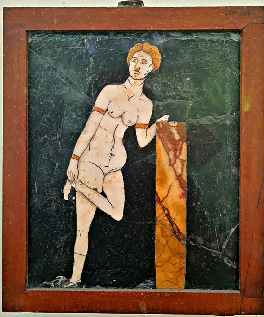 .2.10 Pompeii. Found in triclinium. Photo courtesy of Giuseppe Ciaramella. September 2024.
Now in Naples Archaeological Museum. Inventory number: 109678.
According to the information card –
Venus. Slate wall panel with polychrome marble inlay work.
The theme shows Venus with her hair tied back, with bracelets on her wrists and arms.
She leans with her right elbow on a small column as she unties a sandal. (Third quarter of the Ist century AD.)
(Venere. Panello parietale di ardesia a intarsi marmorei policromi.
Il soggetto rappresenta une Venere dai capelli legati, con bracciali ai poisi e alle braccia, la quale, poggiandosi con il gomito destro a un pilastrino, si slaccia un sandalo. Terzo quarto del I secolo d.C.)