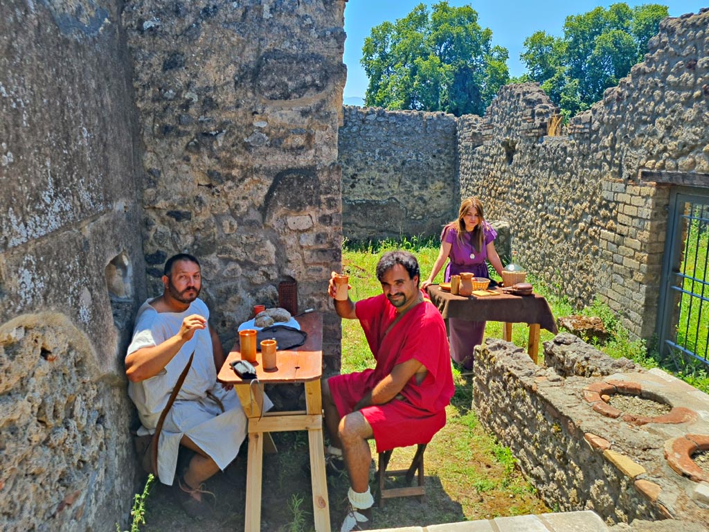 I.2.18 Pompeii. 8th June 2024. Happy customers and serving girl invite customers into bar. Photo courtesy of Giuseppe Ciaamella.
Historical reconstruction entitled L’altra Pompei prende vita (The other Pompeii comes to life).