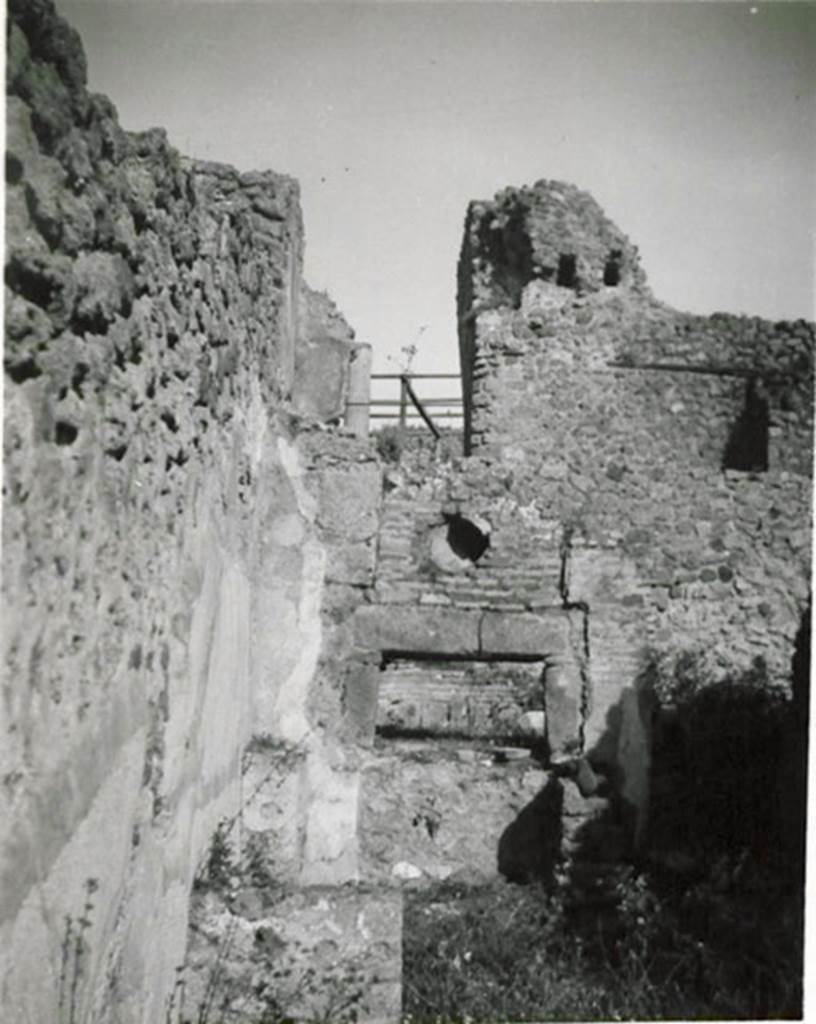 I.3.1 Pompeii. 1935 photograph taken by Tatiana Warscher.
Looking towards oven in north-east corner.
According to Warscher, quoting Fiorelli, “1.3.1. Officina di un pistor dulcarius, che nella taberna prospiciente la via esposti i prodotti lavorati nell’attigua cella, la quale prendeva lume dalla bottega, avendone altra più rozza alle spalle, ed a cui si perveniva passando innanzi al forno; una scala di legno poggiata al muro, ch’è a sinistra della porta, menava alle stanze superiori. Nel foro per il fumo dello forno è incastrata una cornice di terracotta, forse semplicemente un pezzo di anfora. In fondo si vede il muro con fori di traverse della casa No. 3.
(translation: “A workshop of a sweet-pastry maker, that in the shop overlooking the roadway, displayed the products made in the adjacent room, which took its light from the shop, having another rustic room behind, and through which you passed to reach the oven; a wooden ladder rested against the wall, which is to the left of the door, leading to the upper rooms. In the smoke hole in the oven was embedded a terracotta cornice, perhaps simply a piece of amphora. At the rear you see the wall with holes of crossbeams of the house at I.3.3.”)
See Warscher T., 1935. Codex Topographicus Pompeianus: Regio I.3. (no.1), Rome: DAIR, whose copyright it remains.