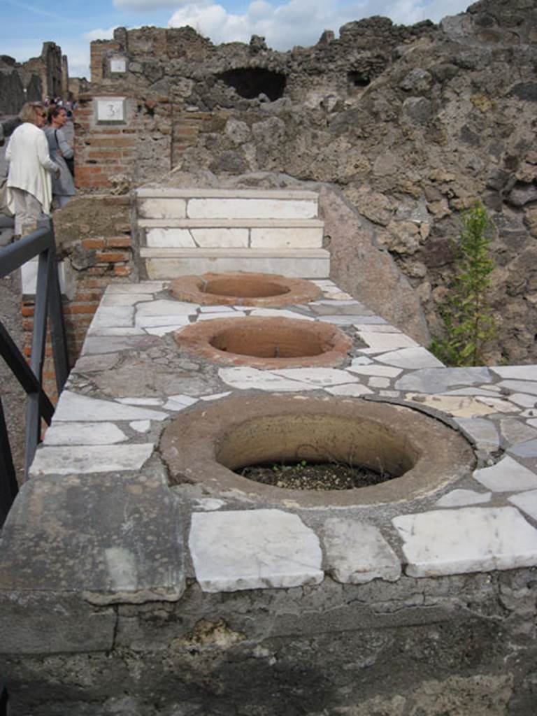I.3.2 Pompeii. September 2010. Looking north along west side of the counter showing three of the four embedded dolia, with Via Stabiana on the left. Photo courtesy of Drew Baker.