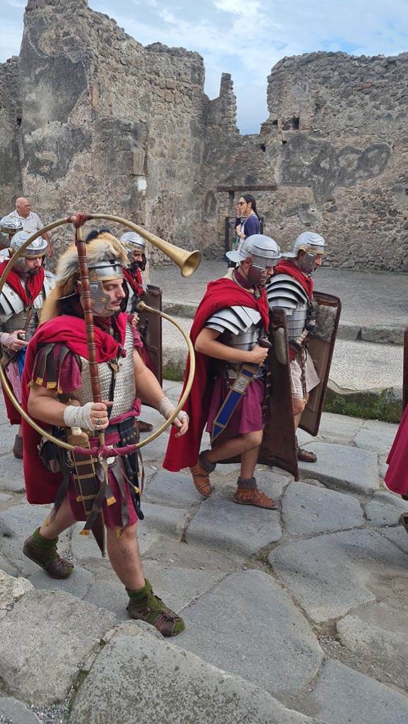 I.4.17 Pompeii. 28th September 2024 during “Ludi Pompeiani” event.
Looking south across Via dell’Abbondanza.
Roman soldiers marching including the “Cornicen” holding a C shaped brass instrument (cornu) used to signal orders to Legions.
Photo courtesy of Giuseppe Ciaramella.