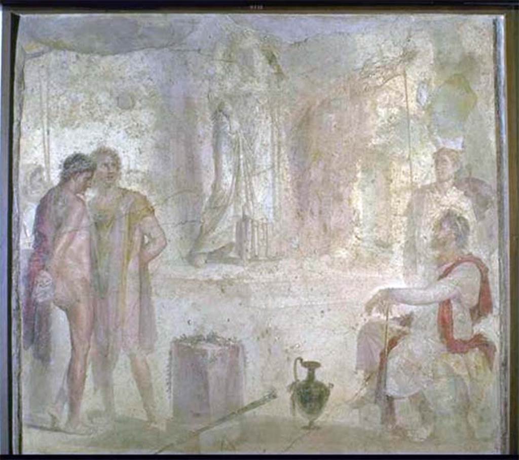 I.4.25 Pompeii. Found 1869. Room 35, east wall of exedra. Wall painting of Iphigenia in Tauris with Thoas, Orestes and Pylades.
According to Helbig, Thoas sits on the right on a stone seat covered with a leopard skin.
Behind him, is a guard wearing a Phrygian cap and bearing a shield in his left hand.
Orestes wearing a red cloak looks melancholy.
Pylades, wearing a yellow and light purple cloak, looks livelier, a mixture of fear and defiance.
A second guard, with face covered and holding two spears, stands behind the prisoners.
At the rear is a staircase that leads to a temple platform on which Iphigenia moves slowly towards the stairs.
The top of the picture is destroyed but it is likely she is looking towards the visitors.
She is probably carrying the Tauran Artemis idol on her left shoulder.
Now in Naples Archaeological Museum. Inventory number 9111.
See Helbig, W., 1868. Wandgemälde der vom Vesuv verschütteten Städte Campaniens. Leipzig: Breitkopf und Härtel, 1333, p. 295-6.