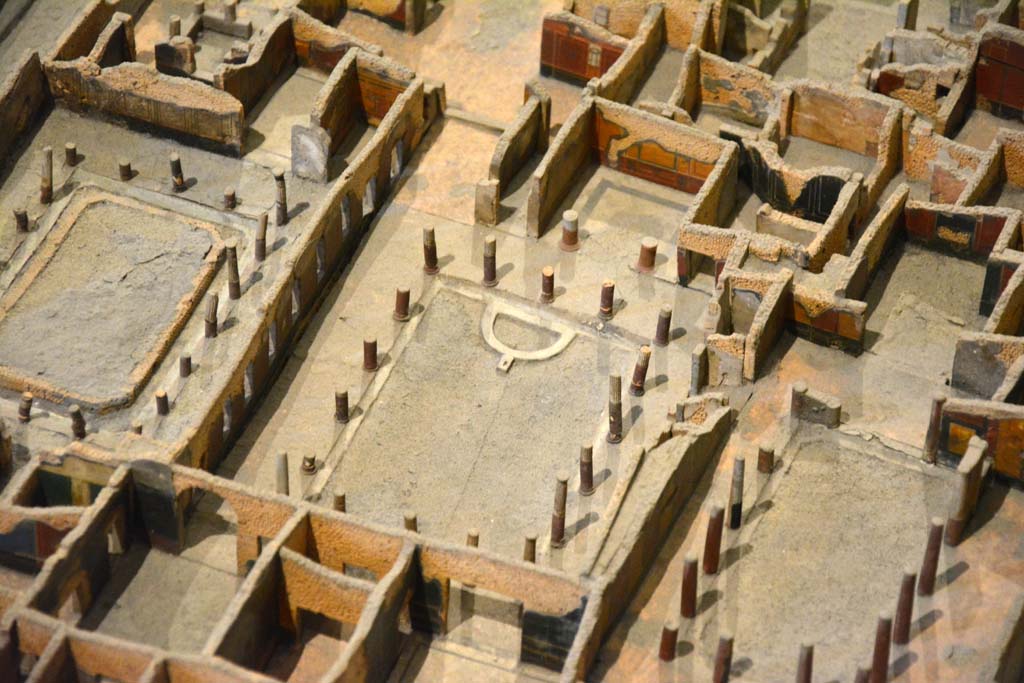 I.4.25 Pompeii. May 2019. Detail from model in Naples Archaeological Museum.
Looking south-west across Middle Peristyle 17, in centre.
Foto Tobias Busen, ERC Grant 681269 DÉCOR
According to Jashemski –
“The centre garden, (the Middle Peristyle), was surrounded by a portico supported by seventeen columns made of brick and Sarno limestone and faced with stucco. The upper parts were fluted, the bottoms left plain and painted red. There was a gutter around the edge of the garden.
At the west end of the garden was a semi-circular basin around which were arranged six spectacular bronze animals found in 1861. …………………………
In February 1926, when restoring the garden in this peristyle, Maiuri discovered a large rectangular pool (3.50m wide x 10.80m long x 1.40m deep). On the west side two high steps (0.45m and 0.40m) led down to the pool. The rough foundations of the much smaller semi-circular pool had been built on these steps and on the bottom of the large pool. The large pool had then been filled with old building material and soil. This was probably at the time that the house with the entrance on the Via dell’Abbondanza was joined to this house, probably after the earthquake. The cistern opening in the south-west corner of the garden had a lava puteal; the one in the east portico, no puteal.”
See Jashemski, W. F., 1993. The Gardens of Pompeii, Volume II: Appendices. New York: Caratzas. (p.29-30).