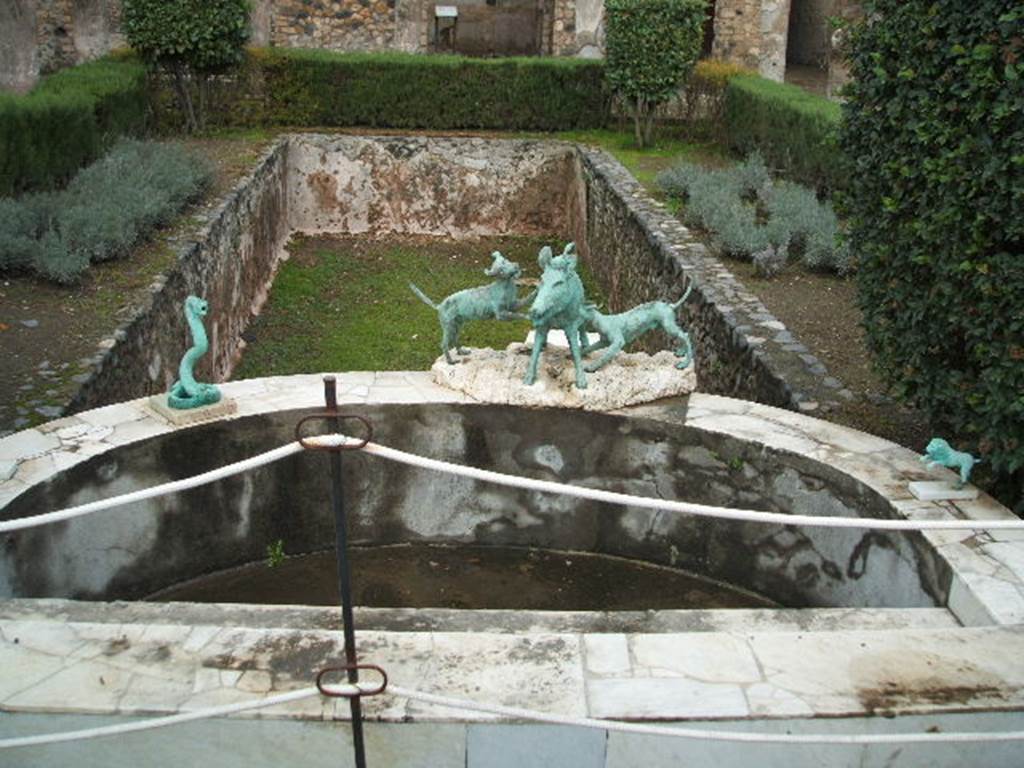 I.4.25 Pompeii. December 2004. Middle Peristyle 17, looking east across semi-circular marble basin and pool.
Around the marble basin are bronze replicas of statues of a cobra, a lion and a boar being attacked by dogs.
The original statues are now in Naples Archaeological Museum.
Remains of Roman lead pipes can be seen in the wall of the rectangular pool.

