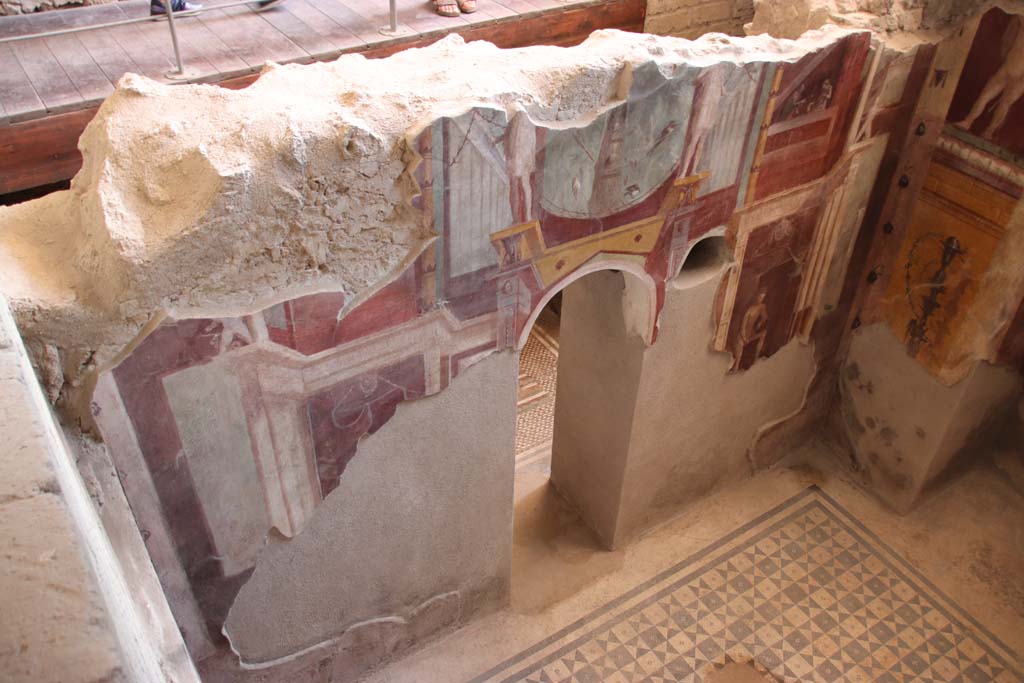I.6.2 Pompeii. September 2019. 
Looking west down on south wall of frigidarium, with arched doorway to anteroom or changing room. Photo courtesy of Klaus Heese. 
In the upper centre zone above doorway is a baetulus [sacred stone] against a background of trees.
The baetulus was chiefly used in connection with the cult of Artemis, in Roman painting.
A baetulus is a sacred stone, derived from a meteorite, which was supposedly endowed with life.


