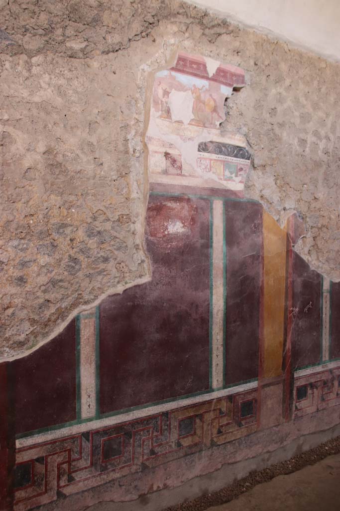 I.6.2 Pompeii. September 2019. Central section of west wall of west wing.
At the top is “the pestilence scene”, which was reconstructed from fragments.
Apollo can be seen with his bow, firing the plague arrows, above the rocks, in the upper left.
The name of the god had been written on the painting in Greek letters (in white below the figure).
People from Achaea pass in the foreground, including a man in a wagon drawn by a donkey, followed by man with a large round shield.
Photo courtesy of Klaus Heese.