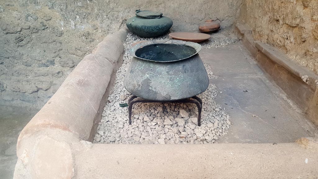 I.6.7 Pompeii. August 2023.
Looking south towards household pots and plates displayed on top of hearth. Photo courtesy of Maribel Velasco.