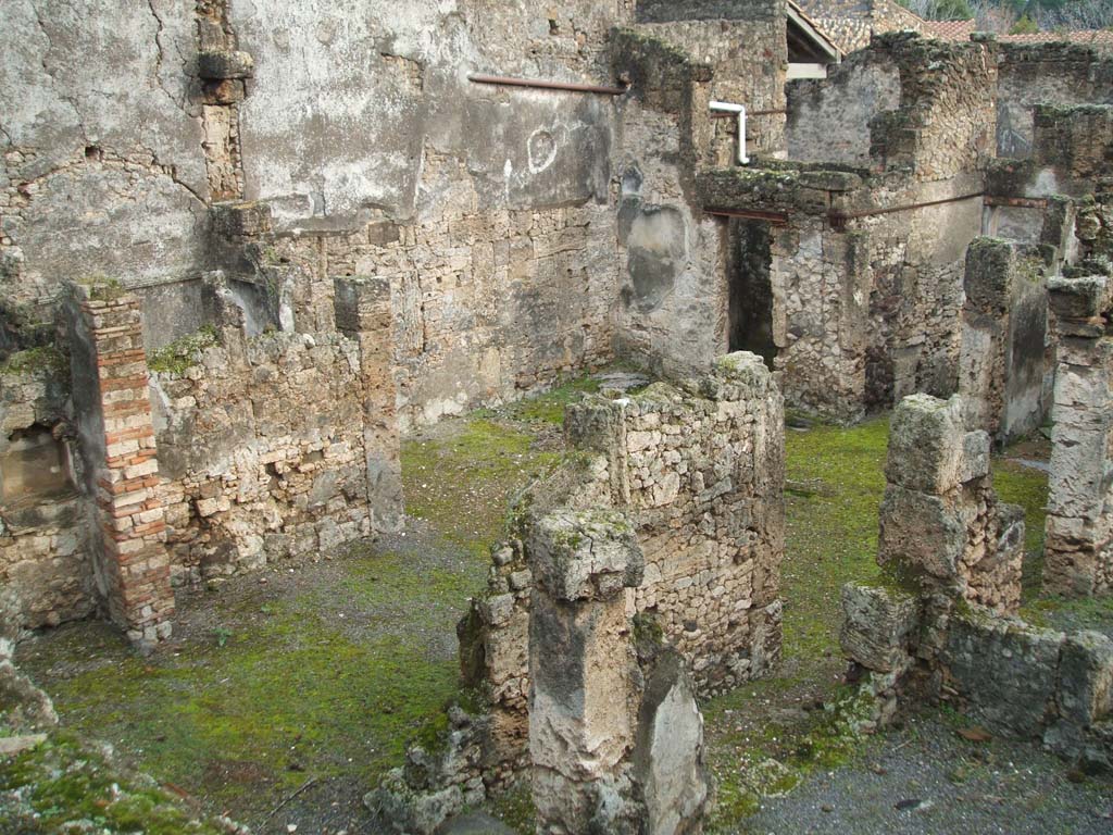 I.6.13 Pompeii. December 2004. Tablinum, atrium and east side looking south-east photo taken from rear of I.6.11.
Behind the east wall of the tablinum, on left, would be the cubiculum (5) in NE corner of atrium.
Room 7 with doorway to corridor “e” is on the lower right, the corridor “e” is on the west side of the tablinum.
The remains of a lararium niche are on left of picture, in garden area behind tablinum.
According to Boyce –
“In the east wall of the garden is an arched niche (height 0.40, width 0.60, depth 0.27, height above the floor 1.30).
This was referred to in the report as “un modesto larario”.
See Boyce G. K., 1937. Corpus of the Lararia of Pompeii. Rome: MAAR 14. (p. 25, no.38)
He quotes reference Not. Scavi, 1929, p.434.