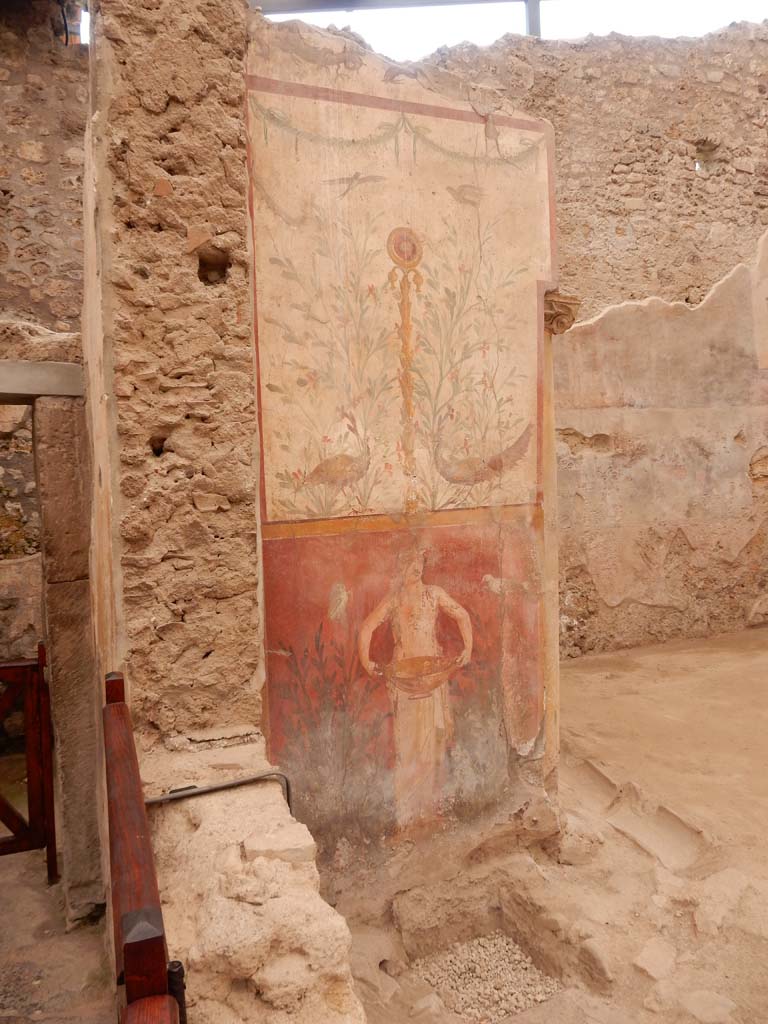 I.6.15 Pompeii. June 2019. Room 9, small garden.
Wall on west side with painting with birds, plants and a medallion above a figure holding a basin or bowl.
Photo courtesy of Buzz Ferebee.