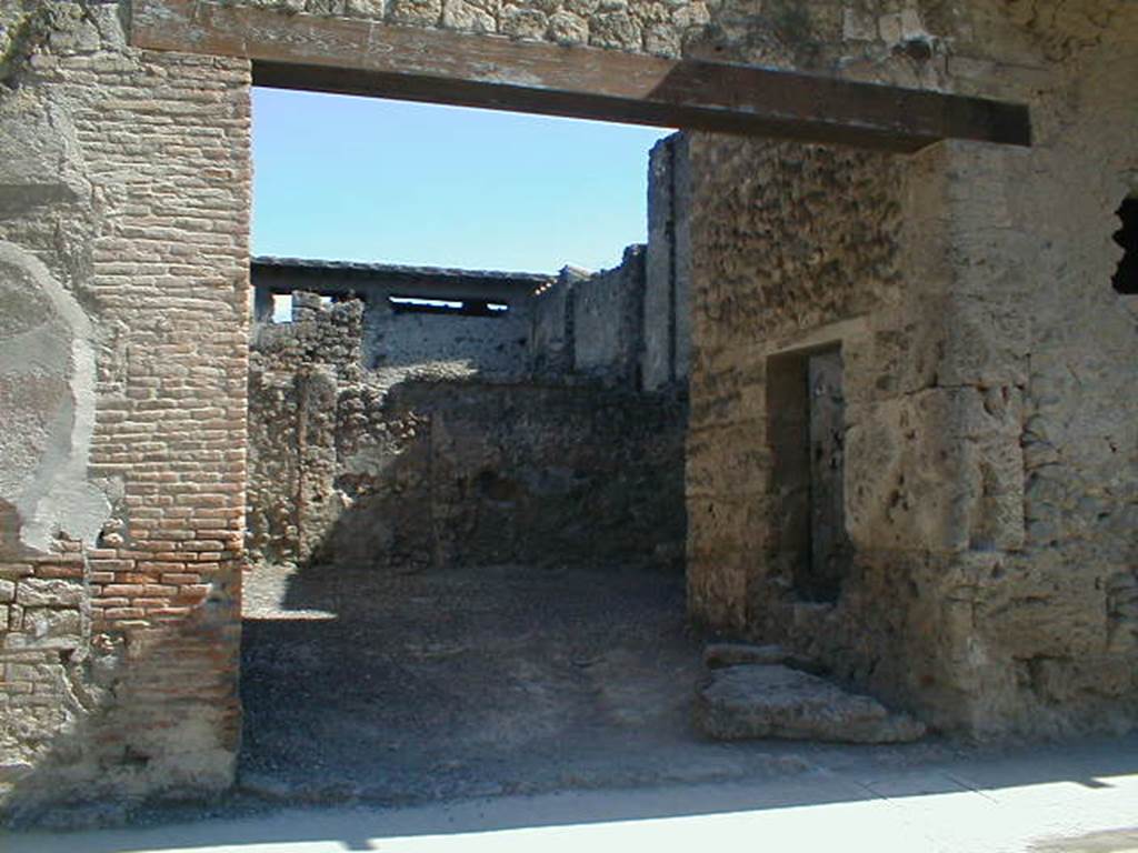 I.7.4 Pompeii. May 2005. Entrance on Via dell’Abbondanza. According to Maiuri, the workshop comprised of a large room on the ground floor, and a smaller room in the north-west corner. This smaller room had a small window in its north wall, onto the roadway, as well as a larger window in its east wall overlooking the vestibule of the workshop.
Against the west perimeter wall was a masonry kitchen area. Found between the kitchen and the rear wall was the recognisable threshold step and traces in the plaster work of a long and steep wooden stairway that would have led up to the upper floor of the room, and from this led both to the balcony and to the other rooms on the upper floor which covered all the space on the ground floor, where there is no trace of an impluvium or possibility of water drainage. Therefore, the roof would have been totally closed and probably only one layer facing the roadway. The walls of the ground floor were simply plastered with a clear yellow background with simple red lines forming squares.
See Maiuri, A., 1928. Nuovi Scavi nella Via dell’Abbondanza. Milano: Hoepli. (p.15-16).
