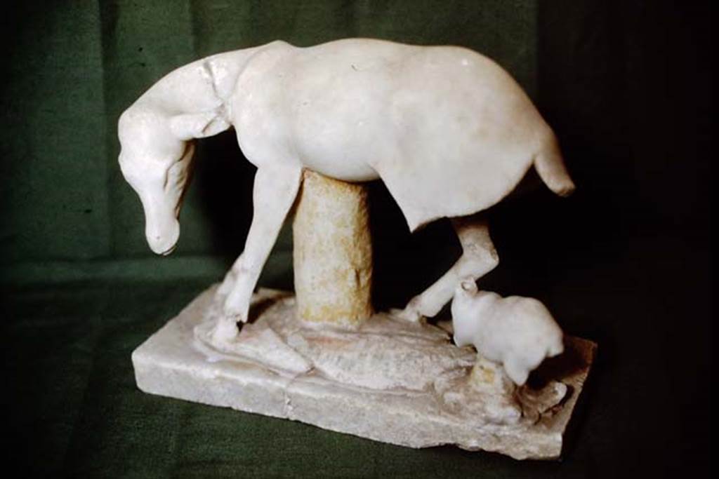 I.7.11 Pompeii, 1978. Statuette of a deer suckling a young faun. Photo by Stanley A. Jashemski.
Source: The Wilhelmina and Stanley A. Jashemski archive in the University of Maryland Library, Special Collections (See collection page) and made available under the Creative Commons Attribution-Non Commercial License v.4. See Licence and use details. J78f0096
This broken statuette was also made of very fine marble and had been gilded. Two other statuettes were also found in the triclinium, one was a headless statue of a white marble satyr, extremely drunk and stretched out on a rock of grey marble. Of the other, only a base of grey marble imitating rocky terrain and showing the goat feet of Pan on a white marble base was found.