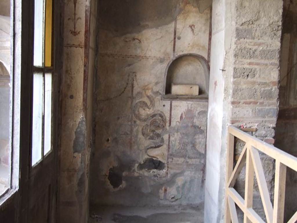 I.7.11 Pompeii. December 2006. Lararium on west wall. According to Boyce, in a very narrow room opening off the north-west corner of the peristyle and west of the triclinium is a lararium. The arched niche is simply decorated with a dark stripe outlining the niche against the white of the surrounding wall. On the wall below the niche are two painted serpents, one on each side. Their heads are on a level with the floor of the niche. (Boyce then gives a note that these serpents direct their heads to the niche as if to receive the offerings placed in it, rather than to the offerings on the burning altar). The serpent on the left is larger and has a red crest and beard, the other serpent being smaller, with neither crest or beard. Between the serpents, under the niche, is a painted flaming altar in the form of a metal brazier. On top of the brazier are eggs. Plants are in the background, and stylized candelabra with festoons border the painting on the sides. Not. Scavi, 1927, 52 with photograph. See Boyce G. K., 1937. Corpus of the Lararia of Pompeii. Rome: MAAR 14. (p.26, no.41B)