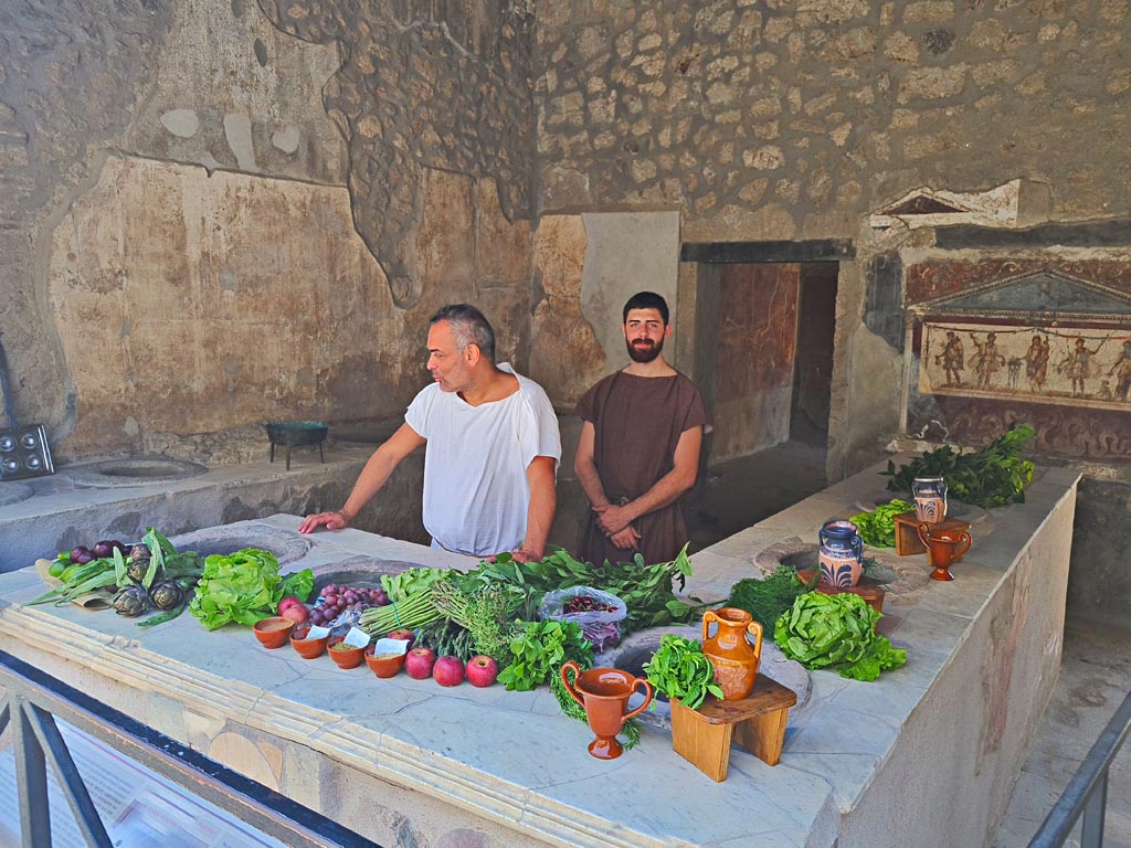 I.8.8 Pompeii. 8th June 2024. Looking south-east across counter fully loaded for customers. Photo courtesy of Giuseppe Ciaramella.
Historical reconstruction entitled L’altra Pompei prende vita (The other Pompeii comes to life).


