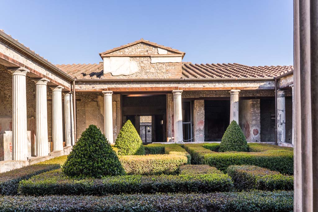 I.10.4 Pompeii. April 2022.
Looking north across peristyle garden from south-west portico towards tablinum, atrium and entrance doorway.
The doorway to room 11 is behind the columns, in the corner on the left. Photo courtesy of Johannes Eber.