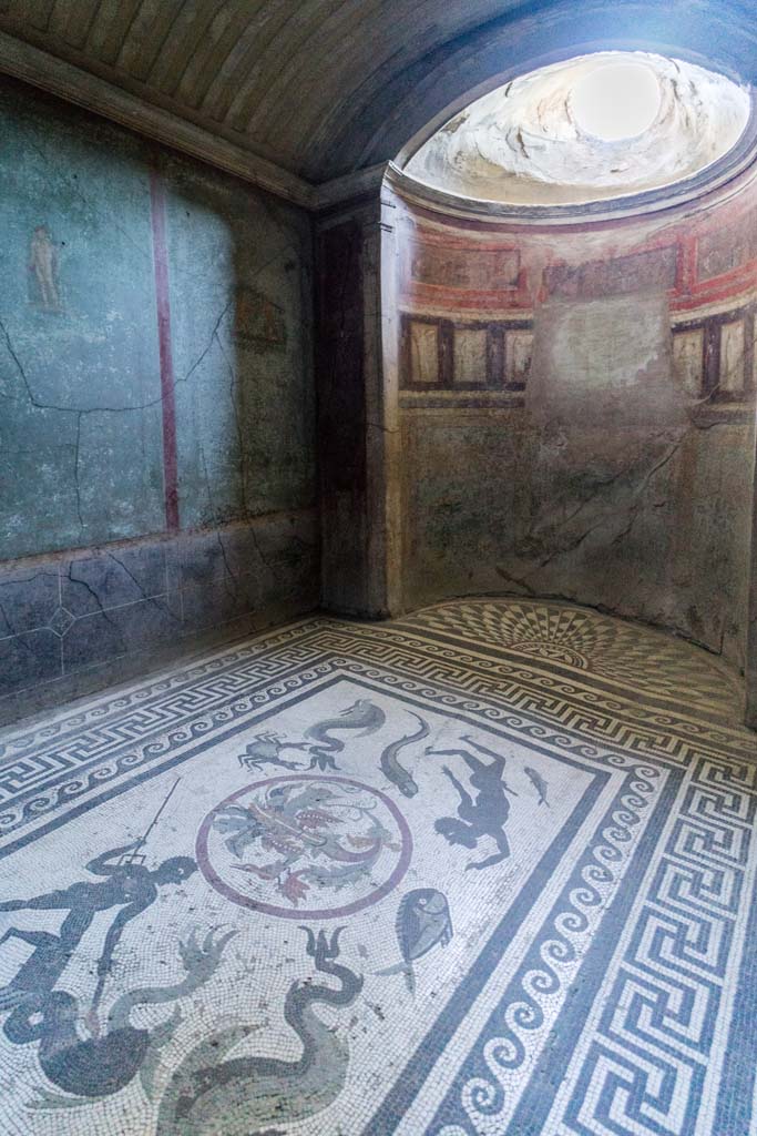 I.10.4 Pompeii. April 2022.
Room 48, looking across ornate mosaic floor with marine theme, towards south-west corner with semi-circular alcove in caldarium (hot room).
Numerous athletic figures decorate the walls. The alcove has painted scenes, painted figures and a window decorated with stucco.
Photo courtesy of Johannes Eber.