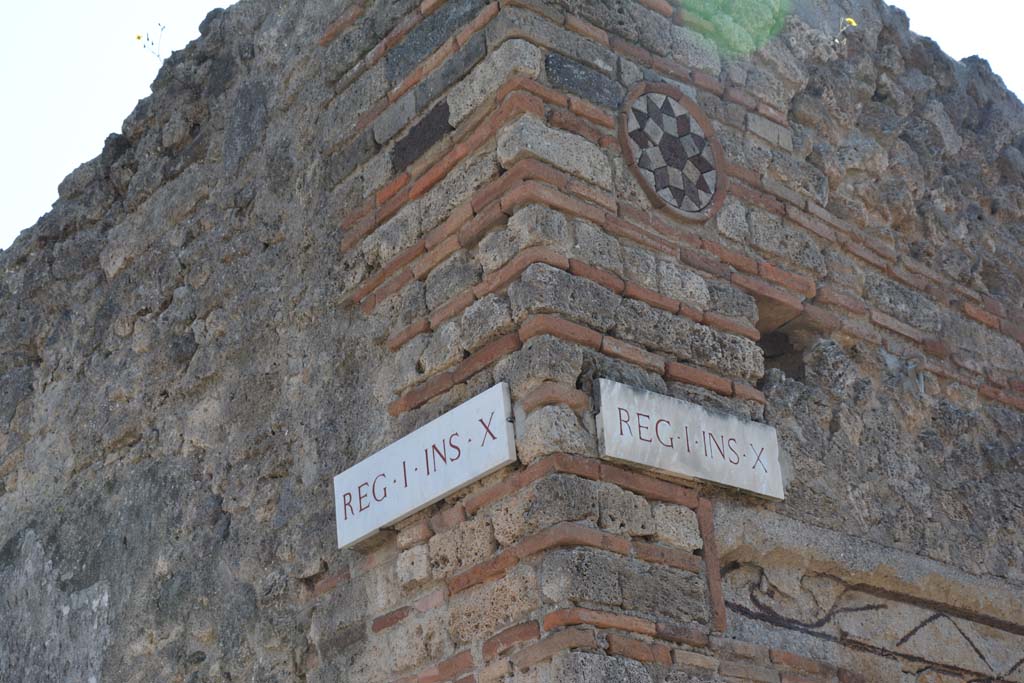 I.10.9 Pompeii. April 2017.
Corner of insula I.10, Vicolo del Menandro, on left, and coloured terracotta plaque above doorway of I.10.9, in Vicolo del Citarista, on right.
Photo courtesy Adrian Hielscher.
