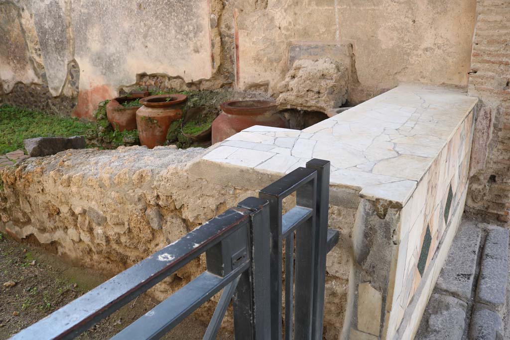 1.11.1 Pompeii. December 2018.
Looking towards west side with remains of four urns and shelves for displaying drinking vessels. Photo courtesy of Aude Durand.