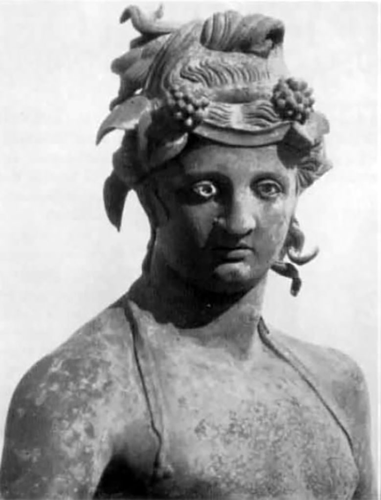 I.16.2, Pompeii. Detail of bronze statue of a young Bacchus.
See Elia, O., 1961. Bacco Fanciullo e Dioniso Chtonio a Pompei: Bollettino d’Arte 1961, Fasc. I-II, (p.2, fig.2).
Kuivalainen comments –
This is another young Bacchus looking absentmindedly elsewhere, and not fully occupied with the activity he is engaged in.
He is pouring wine for a panther, and is perhaps intoxicated himself, as indicated by the position of his legs and the left hand, which once held a thyrsus tightly. The hairstyle may be inspired by Isiac counterparts. (489).
(Note 489 reads – Elia 1961, 2 – 3, suggested that the statue was a product of the eastern provinces).
See Kuivalainen, I., 2021. The Portrayal of Pompeian Bacchus. Commentationes Humanarum Litterarum 140. Helsinki: Finnish Society of Sciences and Letters, (H15, p.220).