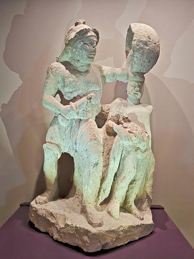 I.20.1 Pompeii. Photo taken May 2021 in Naples Archaeological Museum.
Tuff statue of gladiator with Priapus. Pompei Parco Archeologico inv no: 11739.
Photo courtesy of Giuseppe Ciaramella.
