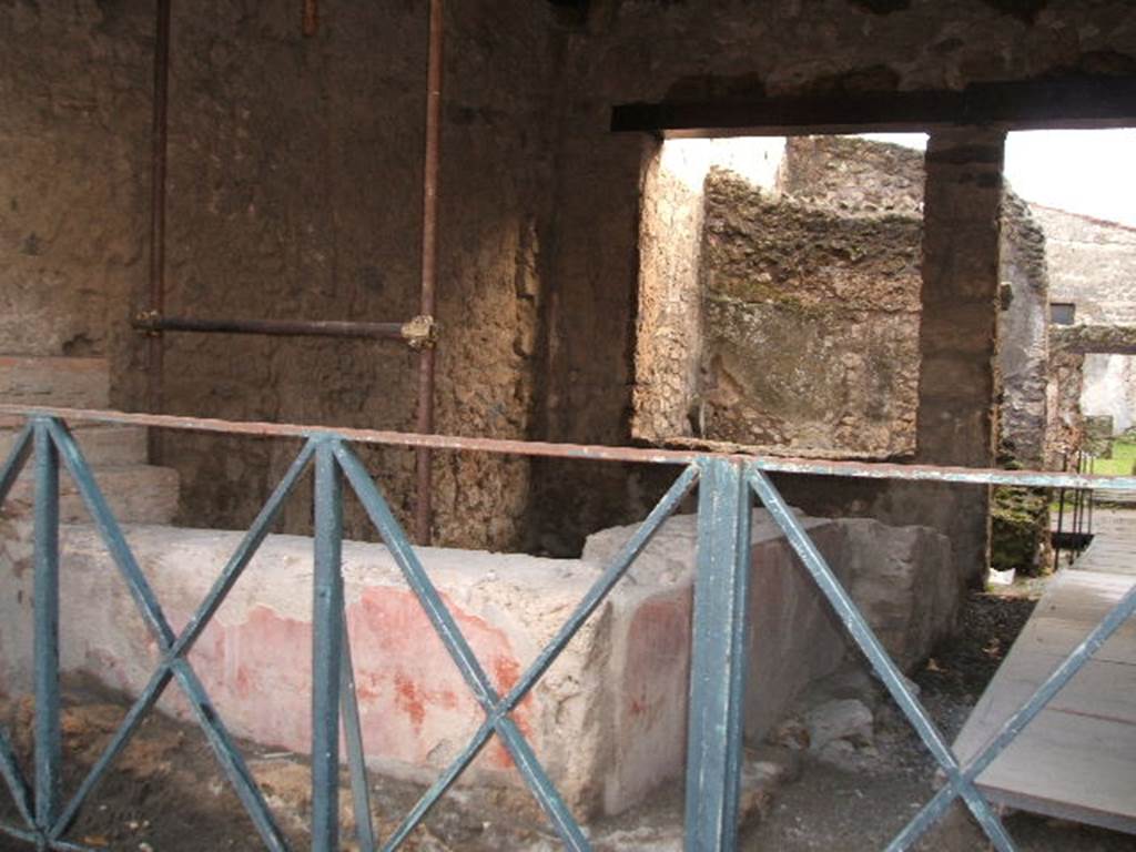 II.1.1 Pompeii. December 2004. Looking south towards two sided counter. According to NdS, the masonry of the counter was covered in stucco, which was painted to imitate a beautiful design of rich polychrome marble inlay. In the centre of the front of the counter was a yellow circle, at the sides of it were two narrow vertical rectangles. These were of white marble veined with green lozenges. At either end of the counter were two narrow vertical rectangles of yellow. At the top, it was finished with a band of white marble.
The base was painted with a red background. The exterior side of the counter was also painted, it showed three large Iris plants with birds flying between them. At the south end of the side counter, a bronze cauldron was found. It was round with a cylindrical neck, and without a lid, it was 0.80 high. Beneath it there was a small hearth. See Notizie di Scavi, 1917, (p.250)
