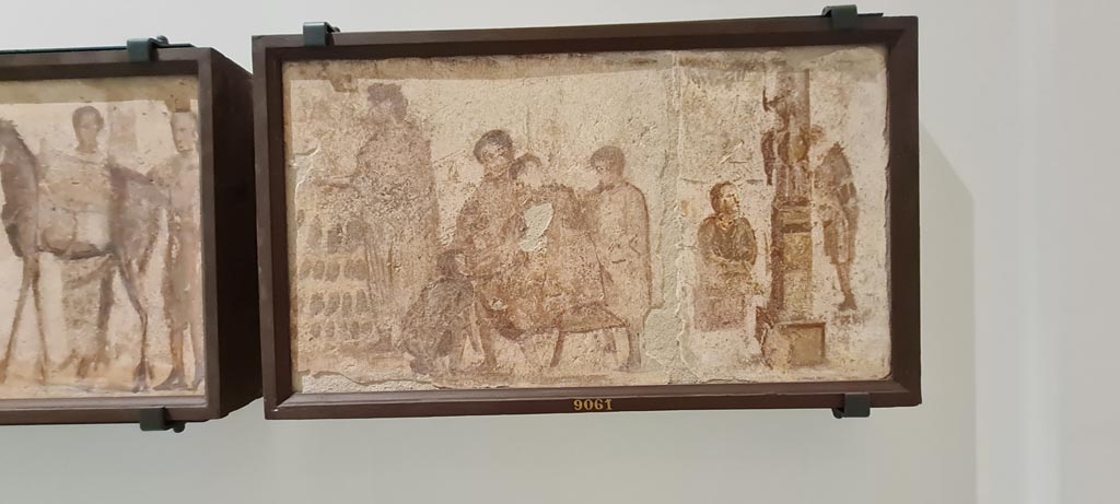 II.4.3 Pompeii. April 2023. Paintings of the Forum frieze, on display in “Campania Romana” gallery in Naples Archaeological Museum.
In centre (inv. 9061) – Vendita di scarpe; scriba e statua equestre.
(Sale of shoes; scribe and equestrian statue). Photo courtesy of Giuseppe Ciaramella.