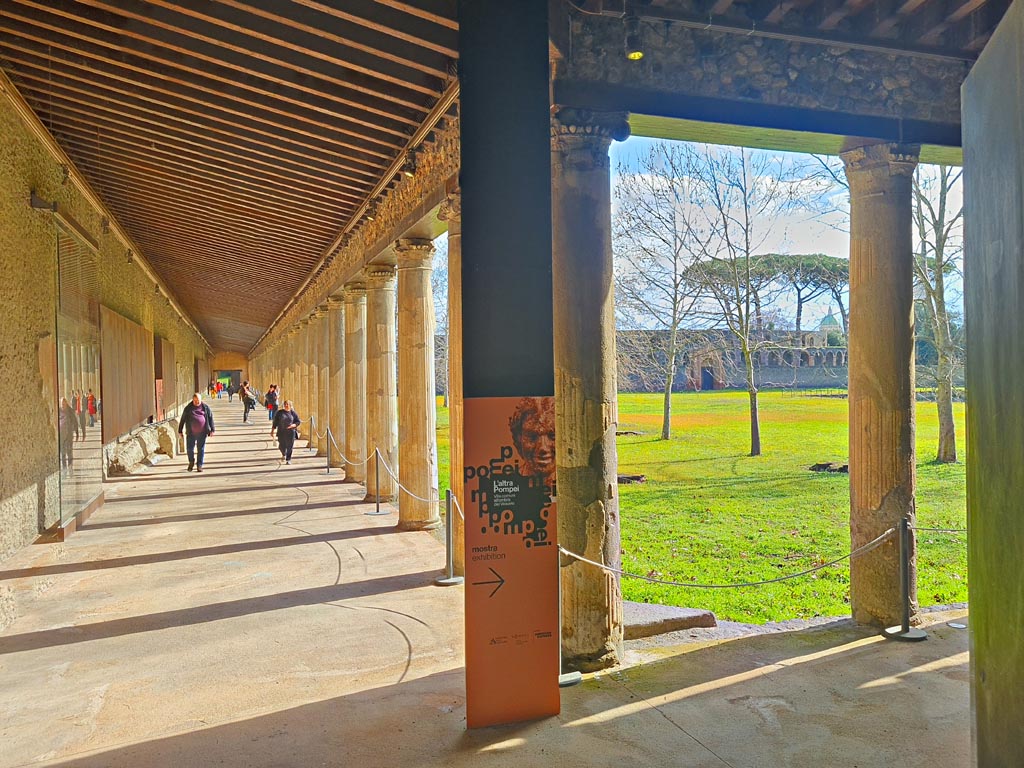 II.7.8 Pompeii. March 2024.
Looking east along north portico, with advertisement for exhibition, signed to the right. Photo courtesy of Giuseppe Ciaramella.