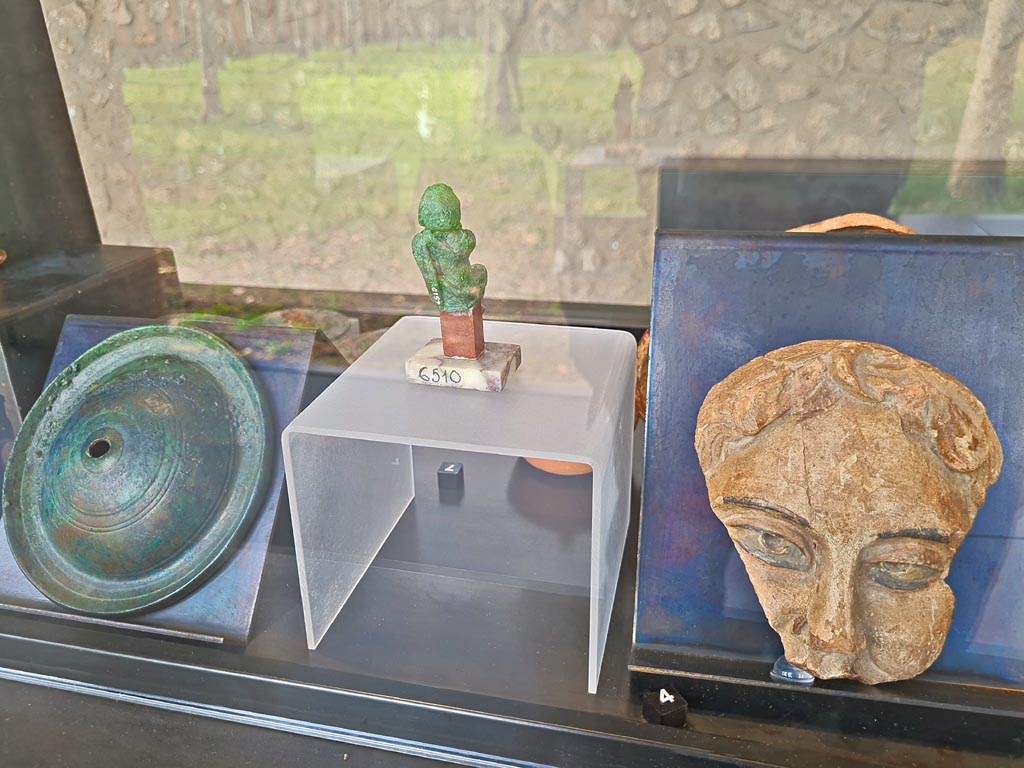 II.7.9 Pompeii. Palaestra. Rear of above cabinet, on display in exhibition in Palaestra entitled – “L’altra Pompei, vite comuni all’ombra del Vesuvio”. March 2024.
On left, No.8 – Bronze cymbals from Pompeii.
In centre, rear of No.7 - Bronze statuette of an actor from I.8.17.
On right, No.4 – one of two Terracotta theatre masks from Pompeii.
Photo courtesy of Giuseppe Ciaramella.
