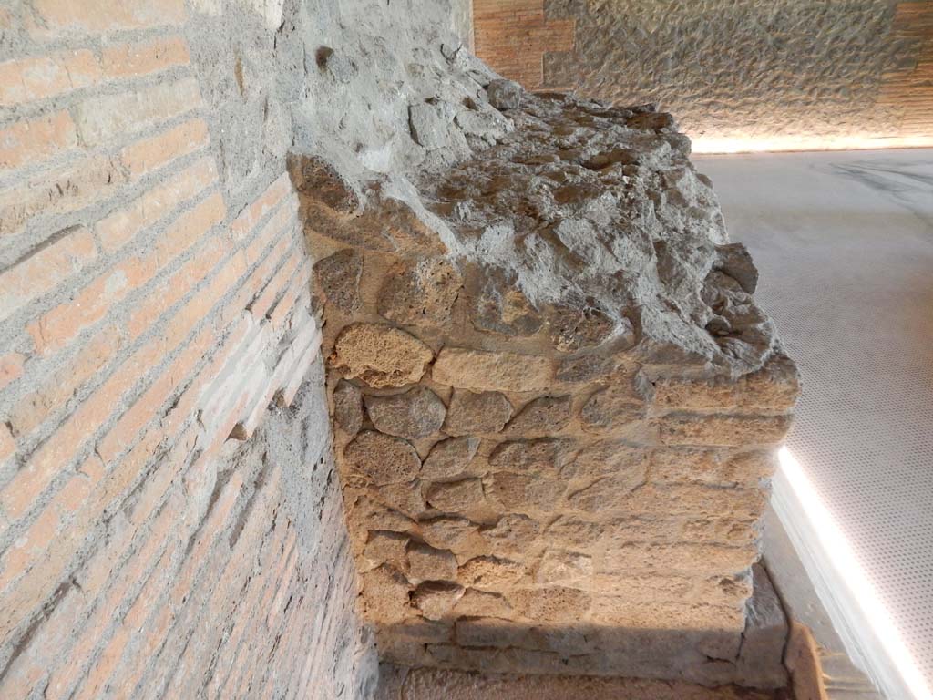 II.7 Pompeii. June 2019. Looking north at remains of marble clad base against west wall.
Photo courtesy of Buzz Ferebee.