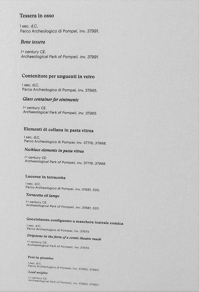 II.9.4 Pompeii. May 2018. Room 8, display list. Photo courtesy of Buzz Ferebee.
Bone tessera (Tessera in osso), inv.no. 37991
Glass container for ointments (Contenitore per unguenti in vetro), inv.no. 37965
Necklace elements in pasta vitrea (Elementi di collana in pasta vitrea), inv.no. 37716, 37968
Terracotta oil lamps (Lucerne in terracotta), inv.no. 37681, 520
Dripstone in the form of a comic theatre mask (Gocciolatoio configurato a maschera teatrale comica), inv.no. 37674
Lead weights (Pesi in piombo), inv.no. 37963,37990
All inventory numbers from Archaeological Park of Pompeii.