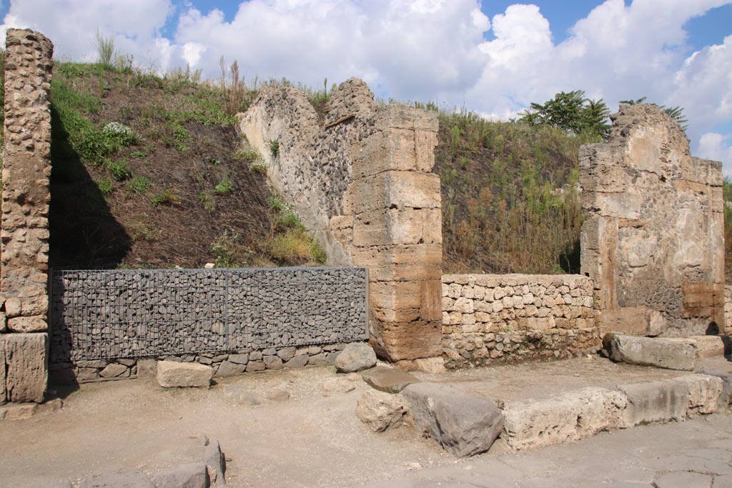 III.7.1, on right, Pompeii. October 2022.
Entrance doorway on north side of Via dell’Abbondanza, with unexcavated roadway between insulae with grey gabions, on left.
Photo courtesy of Klaus Heese