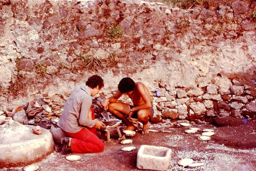 III.7 Pompeii. 1976. Two of Wilhelmina’s helpers, Raffaele and Renato, kneeling down and pretending to cook on the brazier. Photo by Stanley A. Jashemski.
Source: The Wilhelmina and Stanley A. Jashemski archive in the University of Maryland Library, Special Collections (See collection page) and made available under the Creative Commons Attribution-Non Commercial License v.4. See Licence and use details. J76f0478