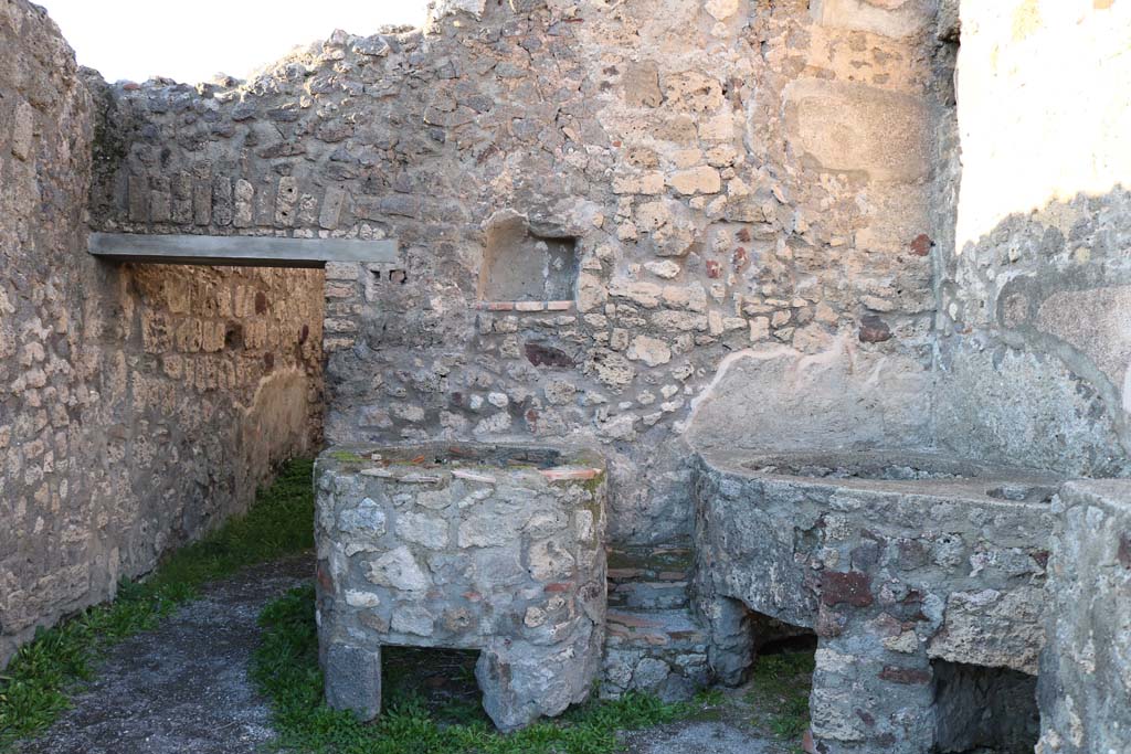V.1.5 Pompeii. December 2018.
Looking towards north wall with doorway to rear room and square niche/recess. Photo courtesy of Aude Durand.