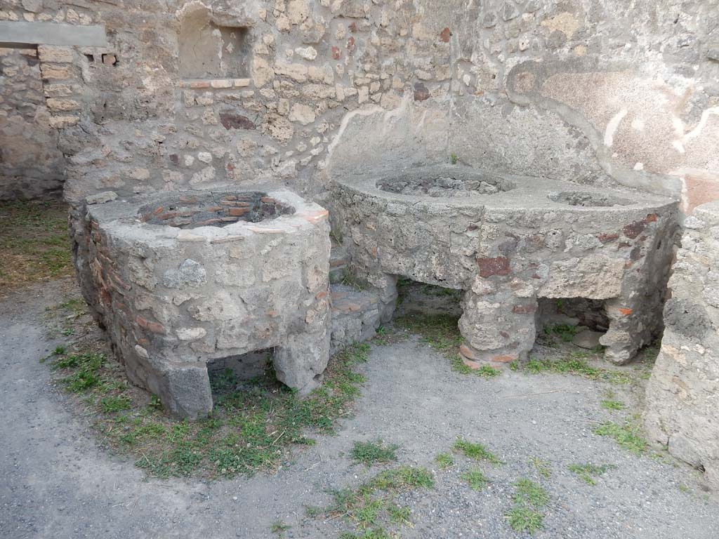 V.1.5 Pompeii. June 2019.
North wall with doorway to rear room, and niche set into wall, with boilers against the north wall and north-east corner.
Photo courtesy of Buzz Ferebee.