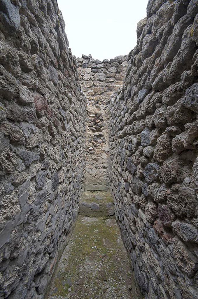V.1.11 Pompeii. c.2005-7? Room “u”, looking north. Photo by Hans Thorwid.
According to Thomas Staub – “This narrow space (0.6 m wide, and 3.4 m long) is in its present state difficult to interpret. It has the appearance of a corridor with a dead end, e.g. ending in the closed north wall. It could either have served as a staircase for an upper floor above the north-western part of the house, but there are no indications or remains of either stairs or an upper floor in the last stage of the life span of the house.”
Photo and words courtesy of The Swedish Pompeii Project.