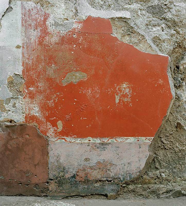 V.1.18 Pompeii. c.2005-2008.
Room “l” (L), detail of painted decoration in centre of lower north wall. Photo by Hans Thorwid.
Photo courtesy of The Swedish Pompeii Project.
Under the central painting of Satyr and a Bacchante in the middle zone of the north wall, was a painted taut garland with head of Silenus and tambourine, in the centre of the red panel.