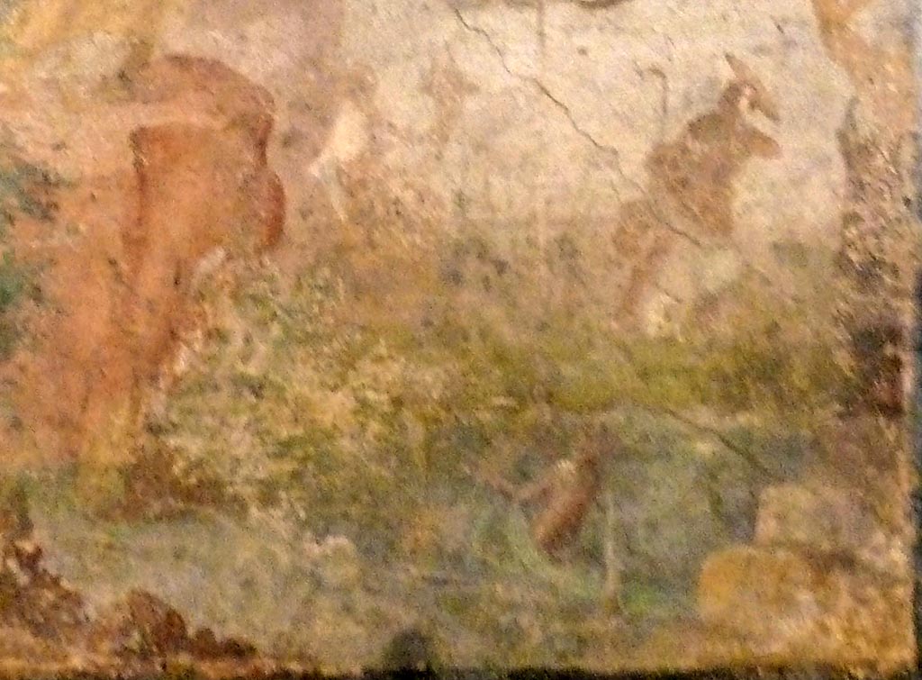 V.2.10 Pompeii. May 2010. Detail from wall painting from east wall of room 9, cubiculum.
Minerva’s helmeted figure, partly obliterated, sits, piping, on a rock near a shrine. Her shield is by her side.
She is looking at an attendant nymph who emerges from the water holding a large mirror which is tilted slightly upwards.
A figure with a cornucopia sits watching nearby.
Now in Naples Archaeological Museum. Inventory number 120626.